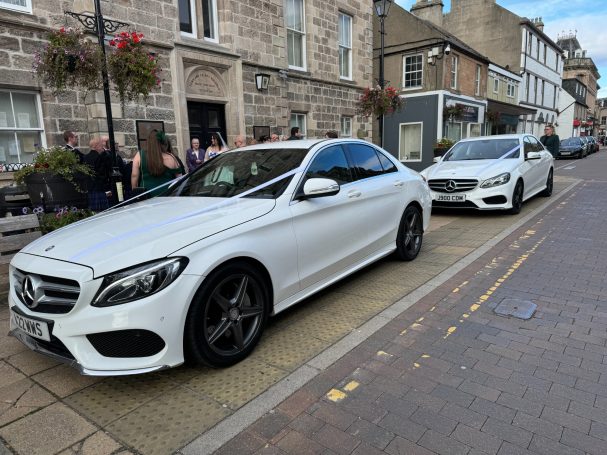 Two of our wedding cars out on hire in Nairn. Two white Mercedes outside the Town House with white ribbon on each vehicle.