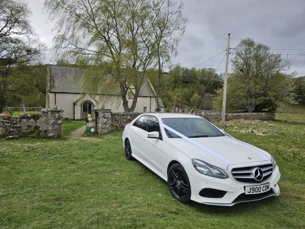 A wedding car at Tomatin Church in Inverness-shire.   A white Mercedes with white wedding ribbon on the vehicle